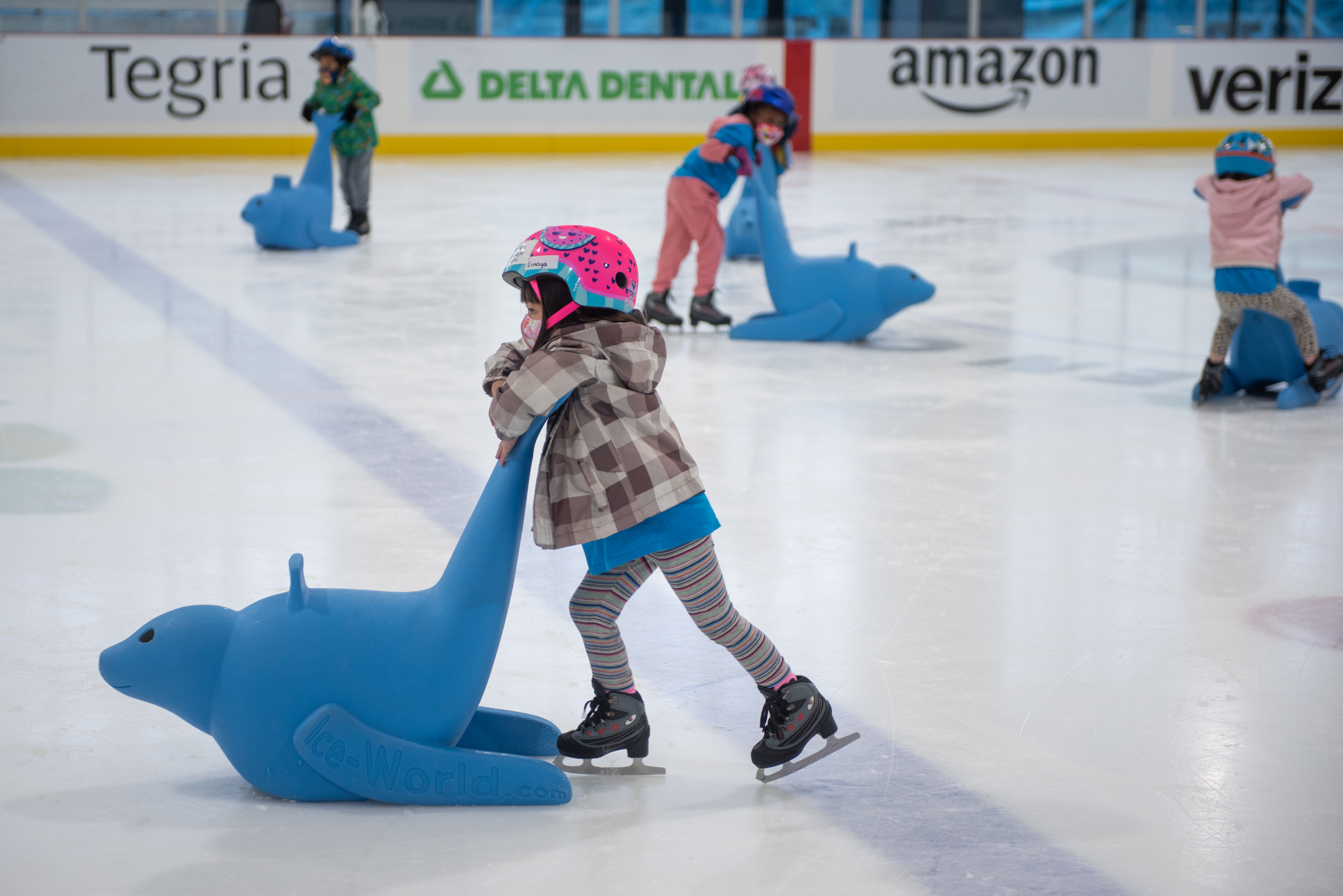 A young skater in rental skates and a helmet pushing a large plastic seal.