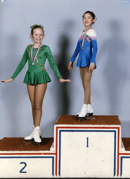 Kristi Yamaguchi stands atop a podium as a young child wearing a figure skating costume.