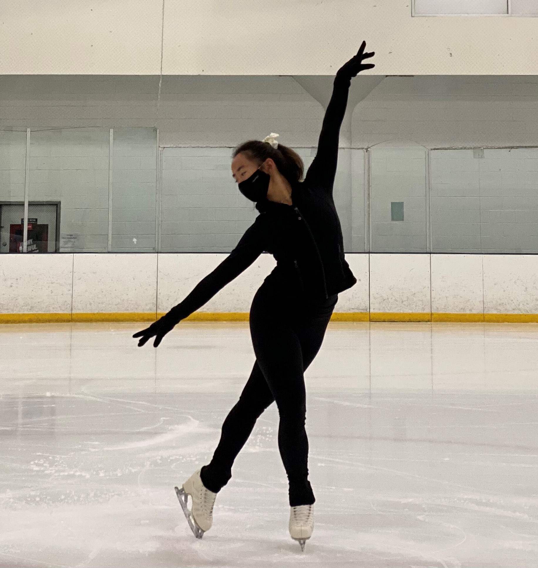 Caroline, in all black and a mask, poses on the ice.