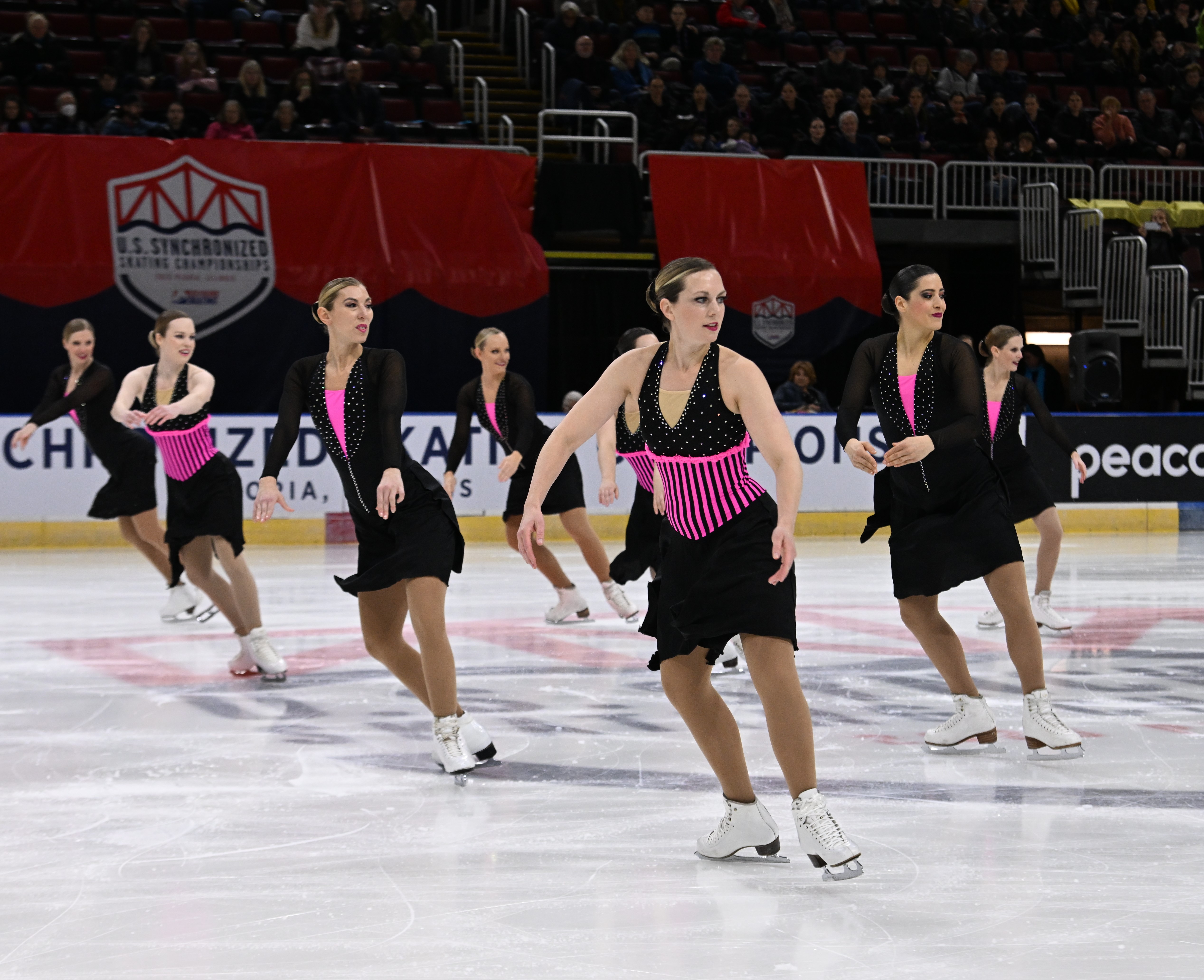DC EDGE adult team competes at the 2023 U.S. Synchronized Skating Championships wearing matching black skating costumes with pink corsets