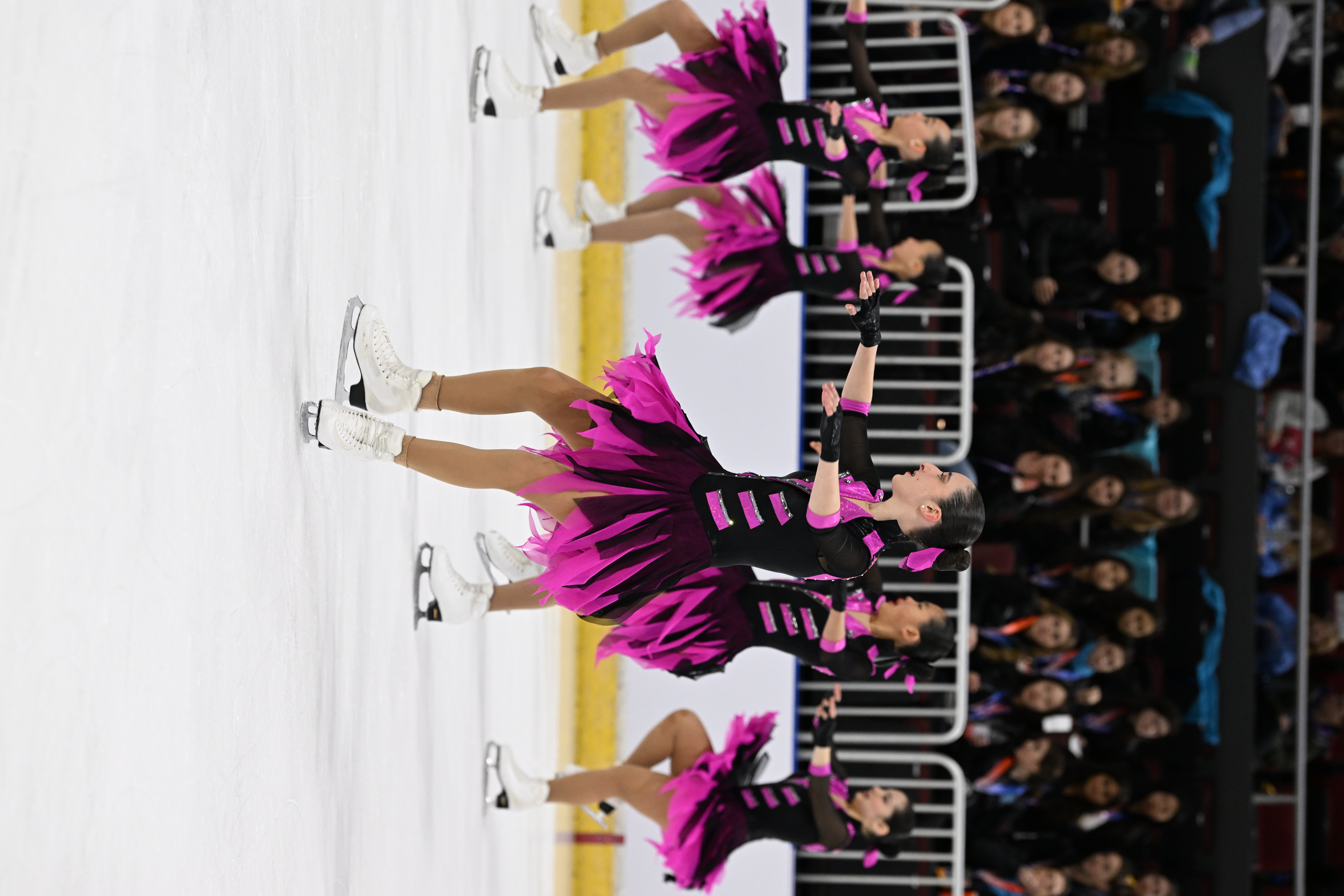 Team Image juvenile executes a spin in unison wearing matching black and pink skating costumes