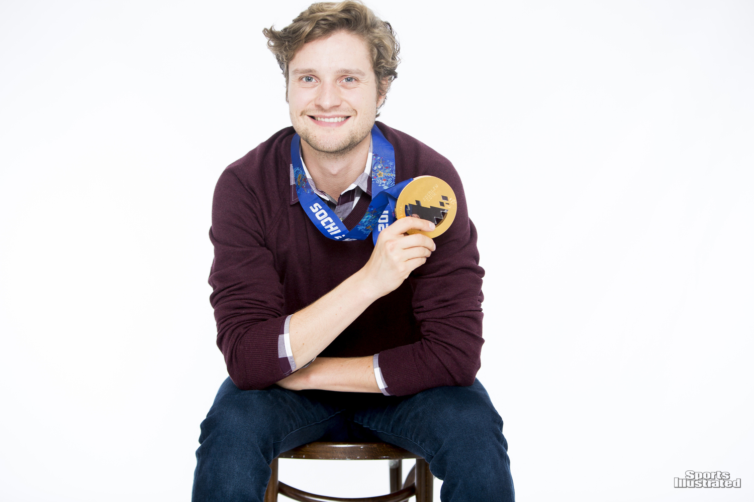 Charlie White sitting down in a red sweater holding his Olympic gold medal.