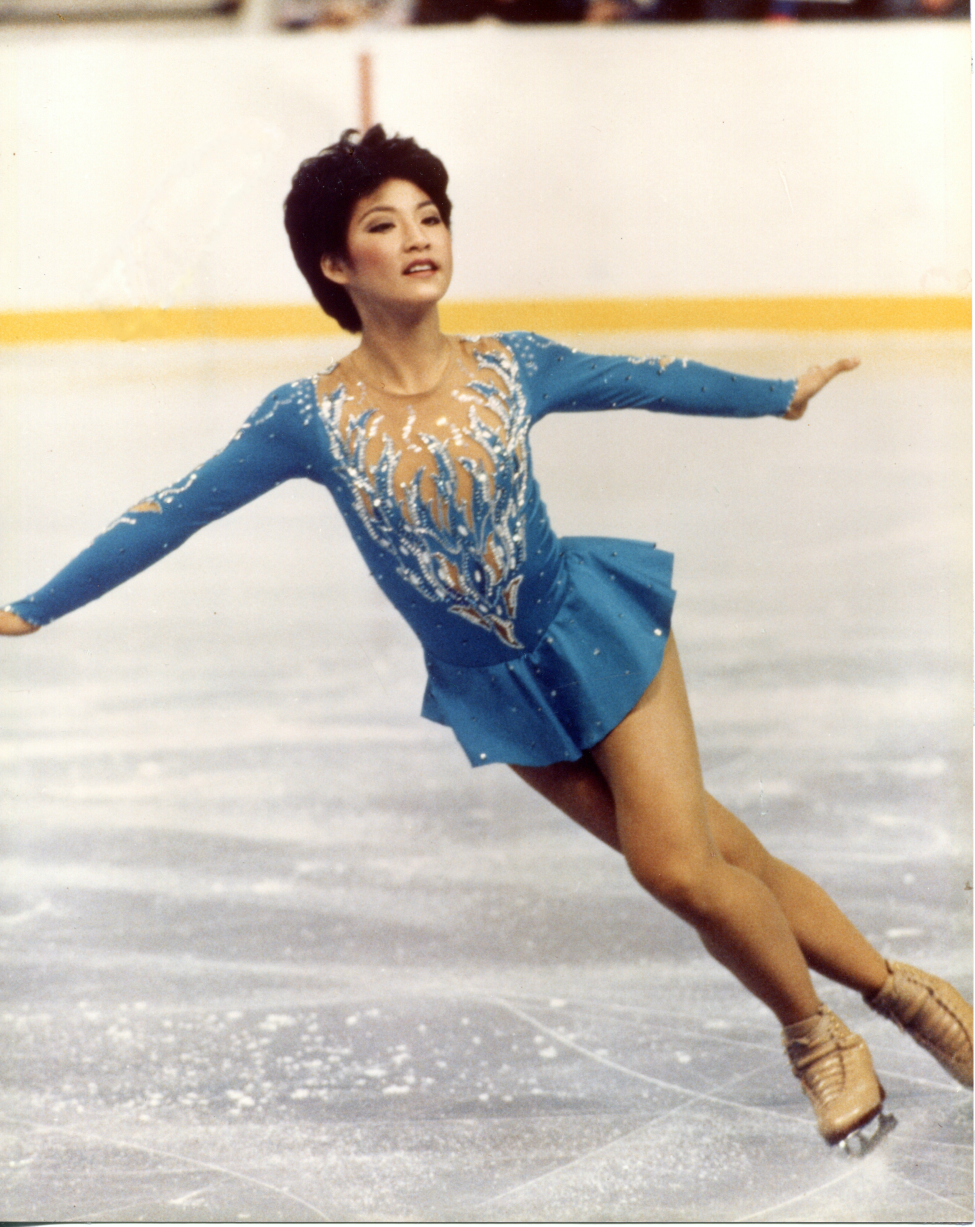 Tiffany Chin skates across the ice donning a short black haircut wearing a light blue retro skating dress.