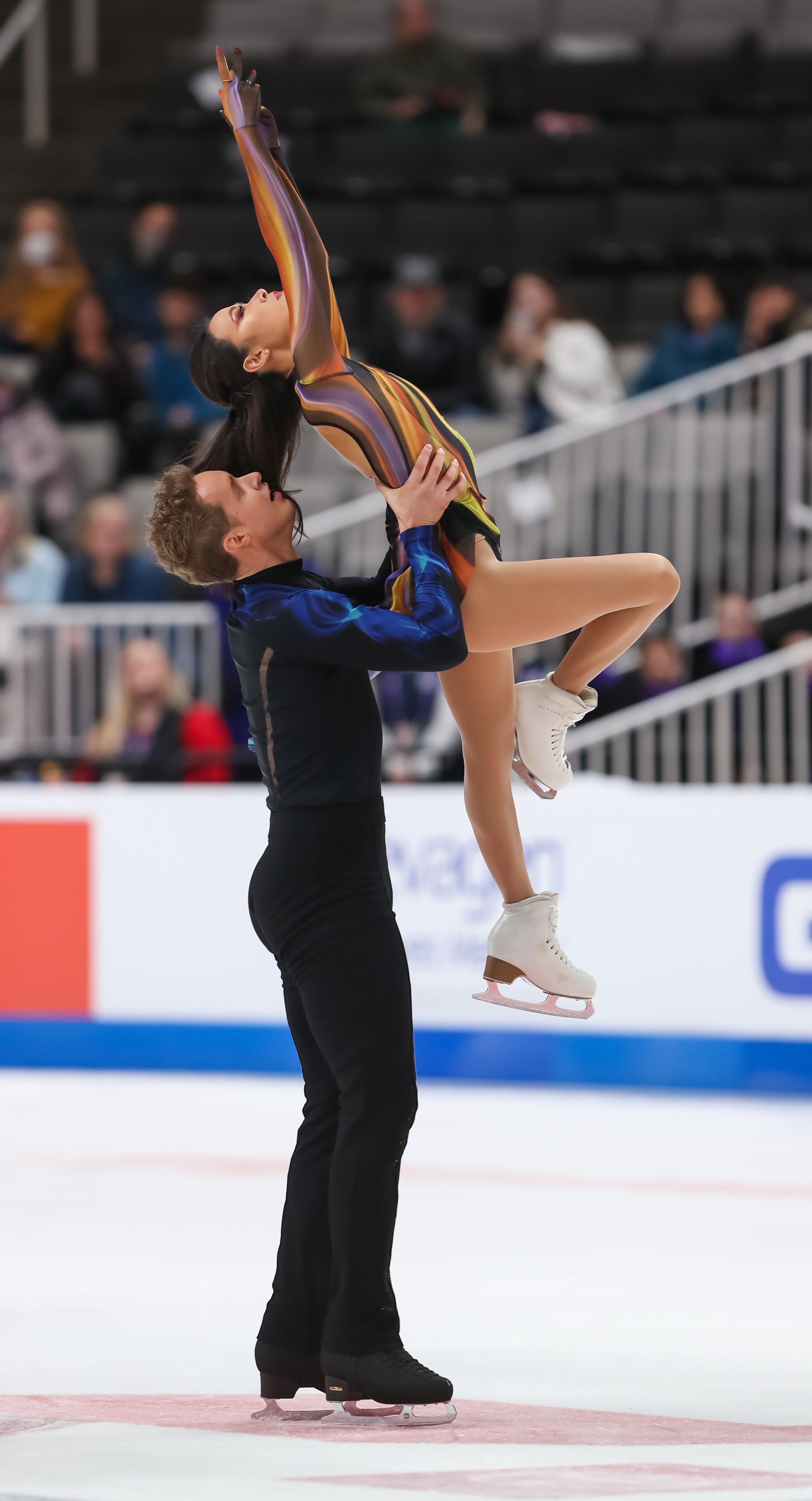 Madison Chock and Evan Bates compete in the free dance at the 2024 Prevagen U.S. Figure Skating Championships. They wear fire and ice inspired costumes. Bates is holding Chock up in the air as she looks and points upwards