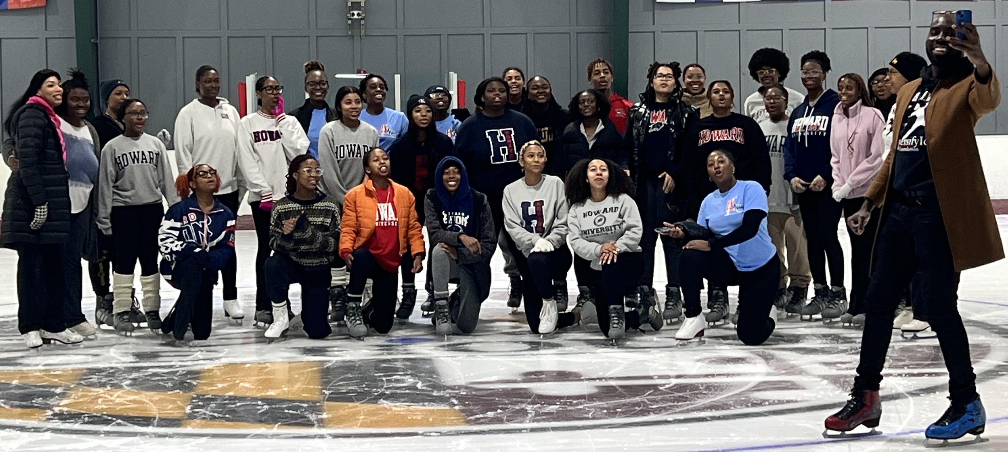 Group photo of the Howard University Figure Skating Team. Joey Savary, a Black man, stands in front of the group taking a selfie. 
