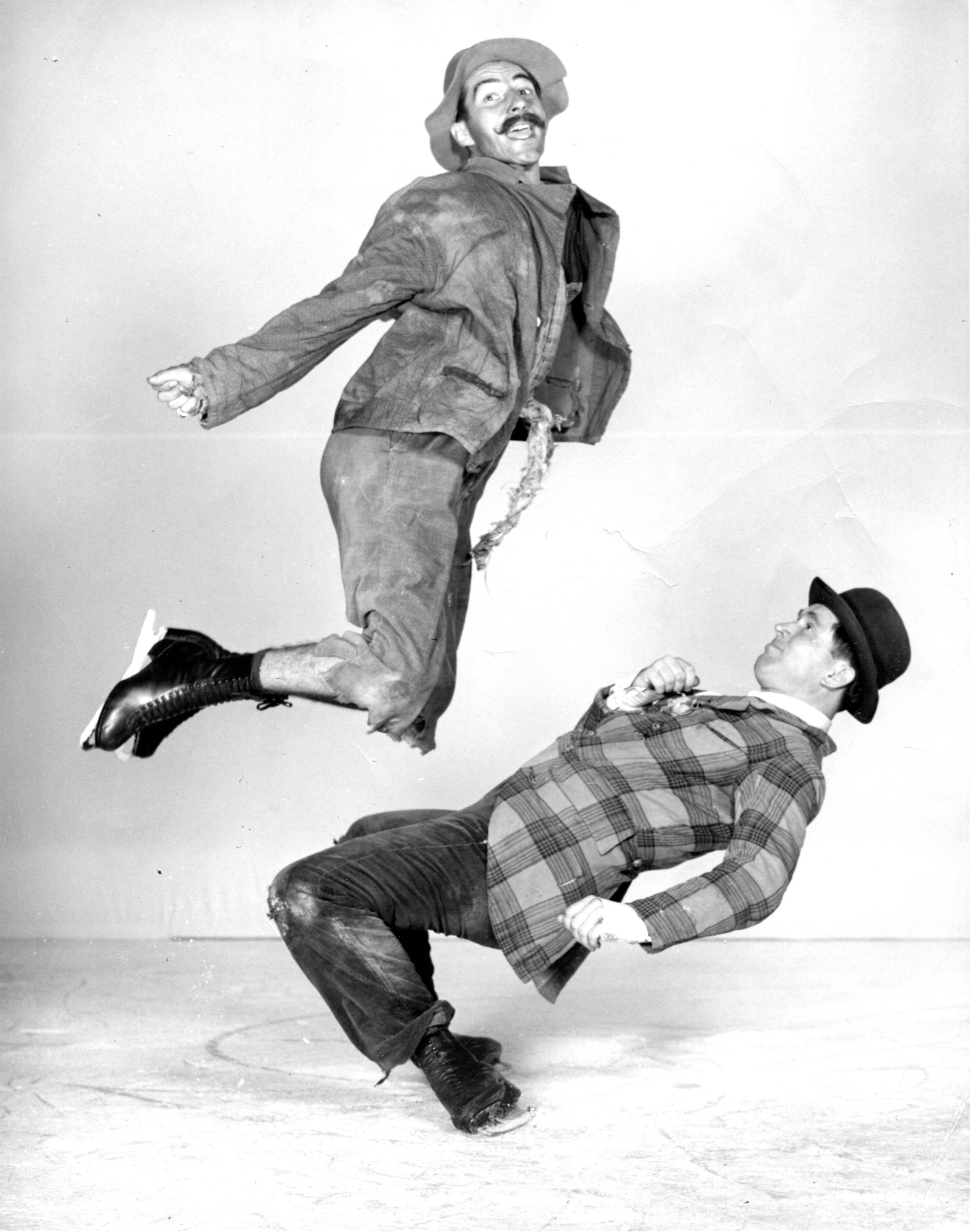 1930s show skaters Frick and Frack perform a jump and duck move in skates in a black and white staged photo.
