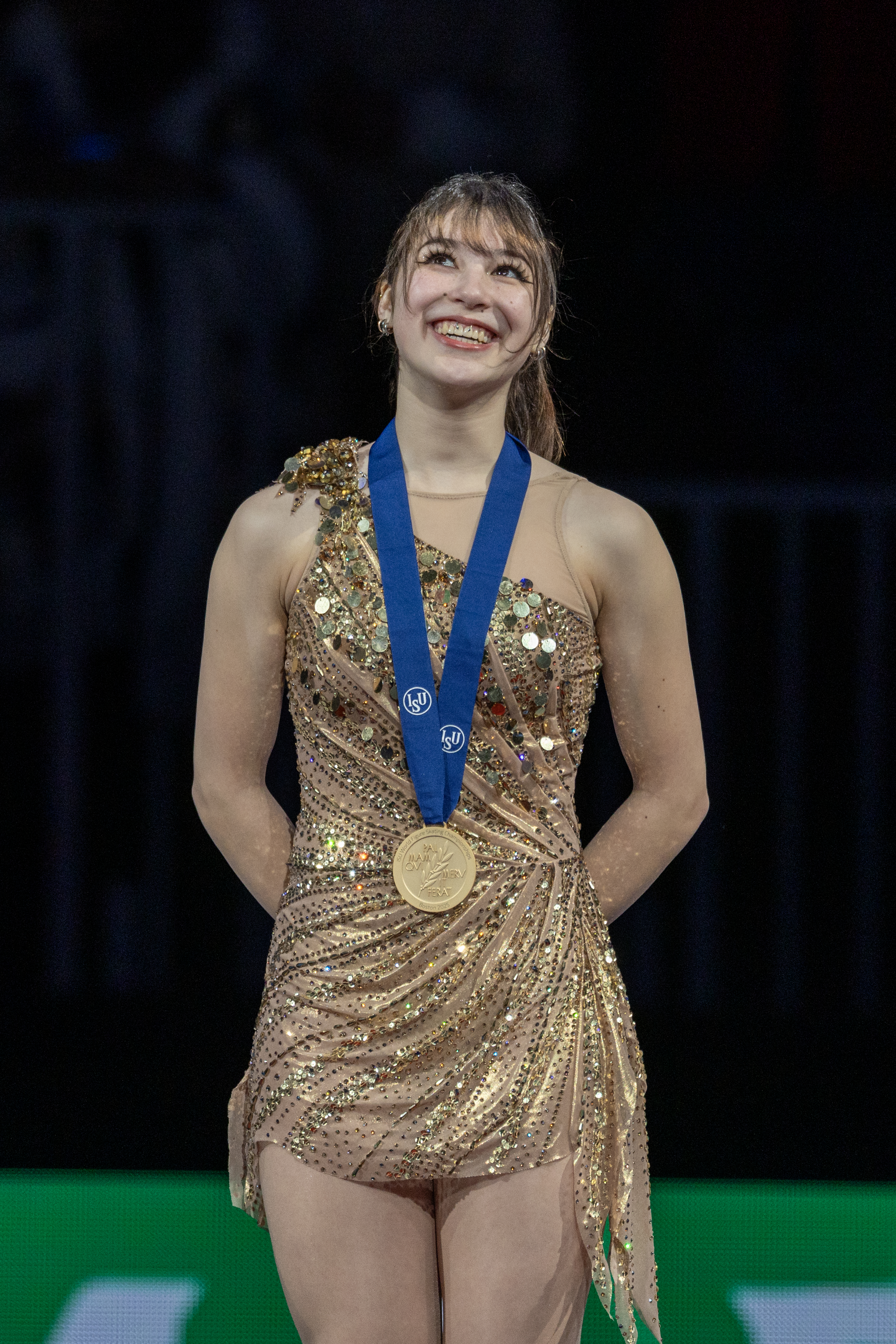 Alysa Liu, dressed in a gold costume, is all smiles as she stands on top of the World podium.