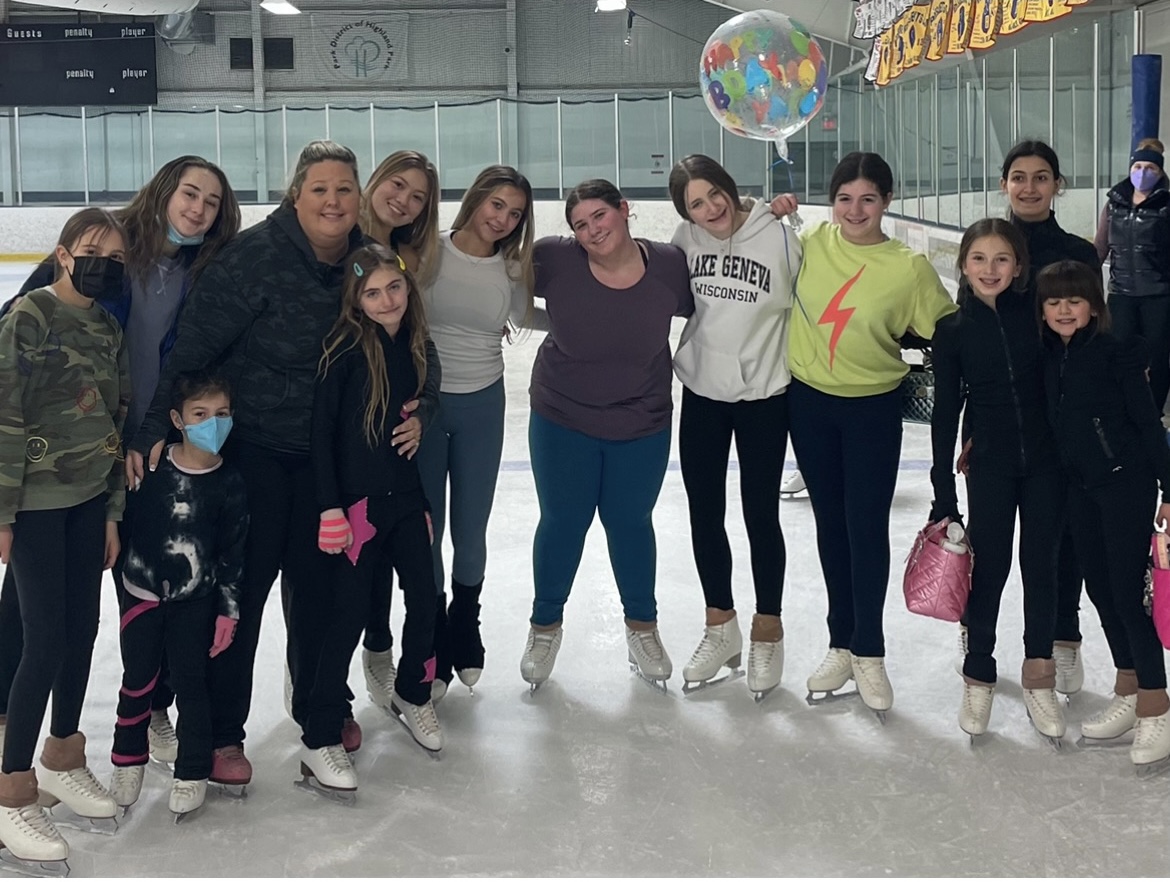A group of skaters pose on the ice together by the rink boards.