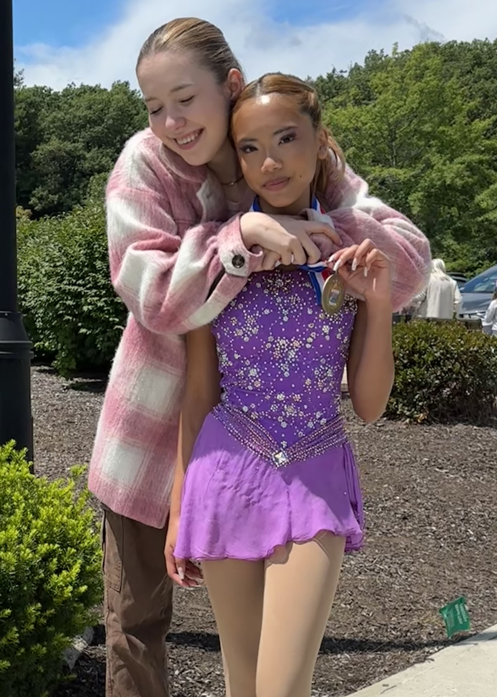 Isobel Carney hugs a young student of her from behind, after winning a medal. The photo was taken outside the arena, on a sidewalk.al. 
