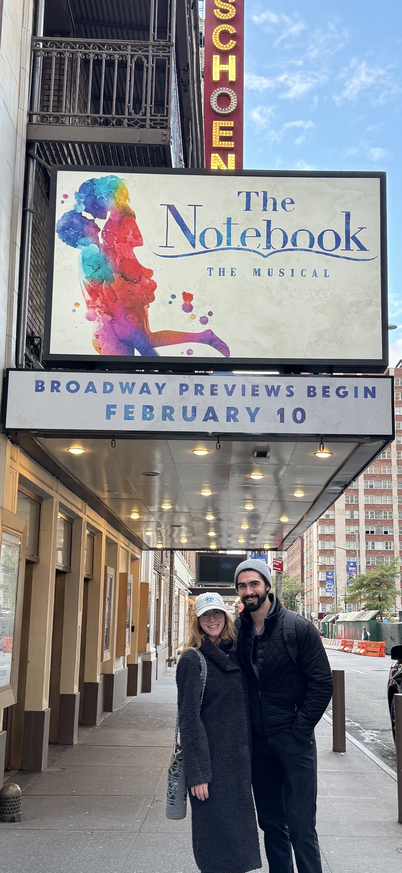 Alex and his wife, Jordan, in front of the Schoenfeld Theatre. A sign for the Notebook is above them.