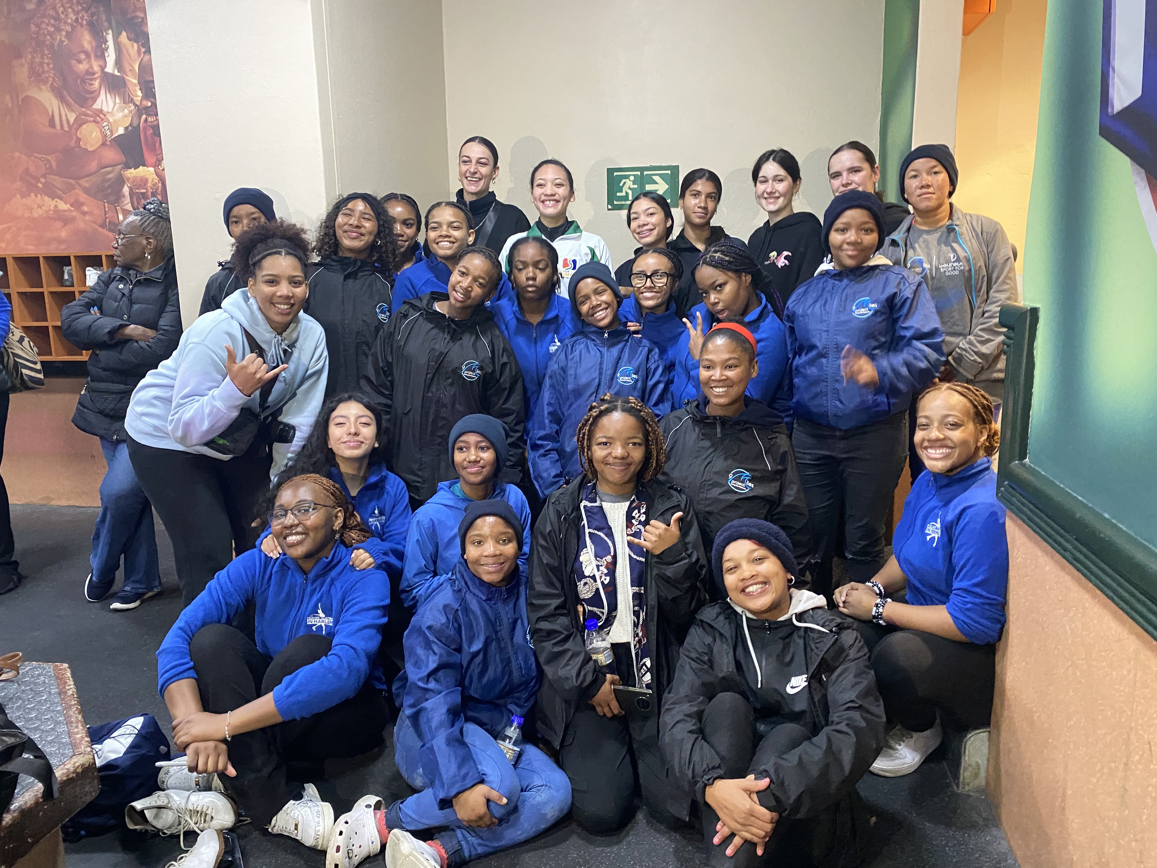 Group photo of Figure Skating in Harlem. Several girls in the photos are wearing blue jackets with the club's logo on the front.