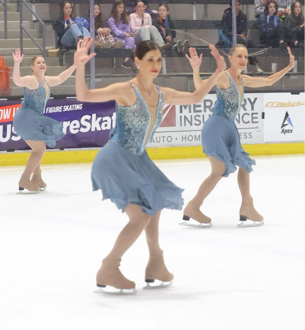 Naomi Lang, wearing a light blue dress, competes with her IceDenettes teammates.
