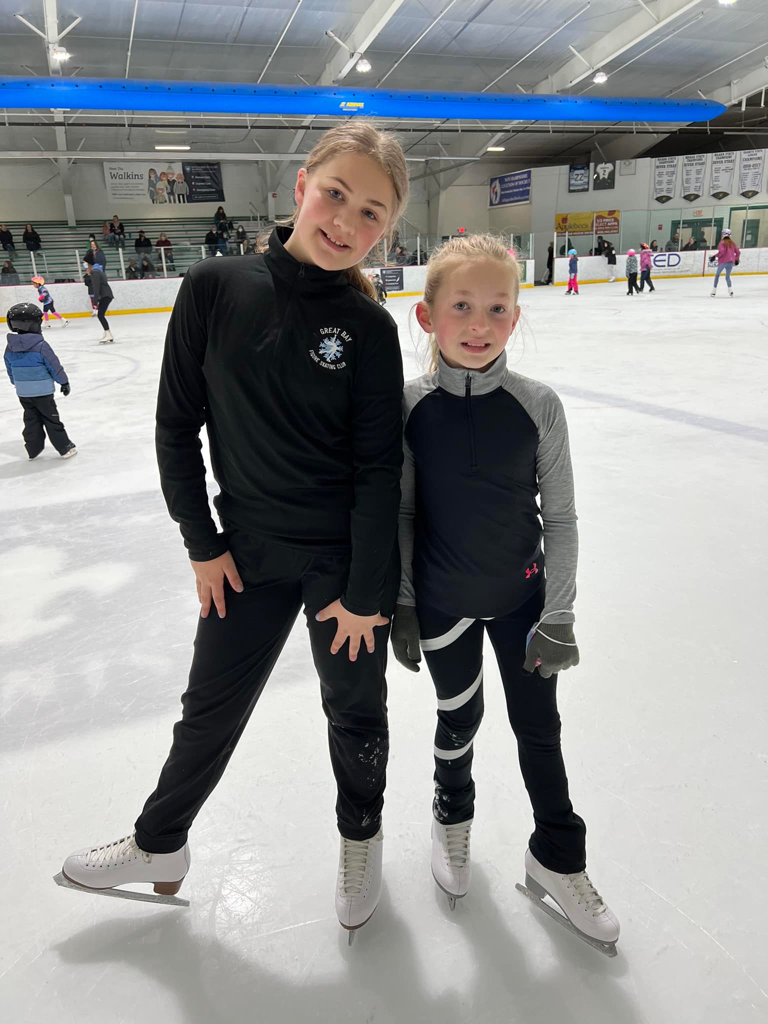 Peyton and Lilly stand in skating practice outfits and black leggings on the ice.