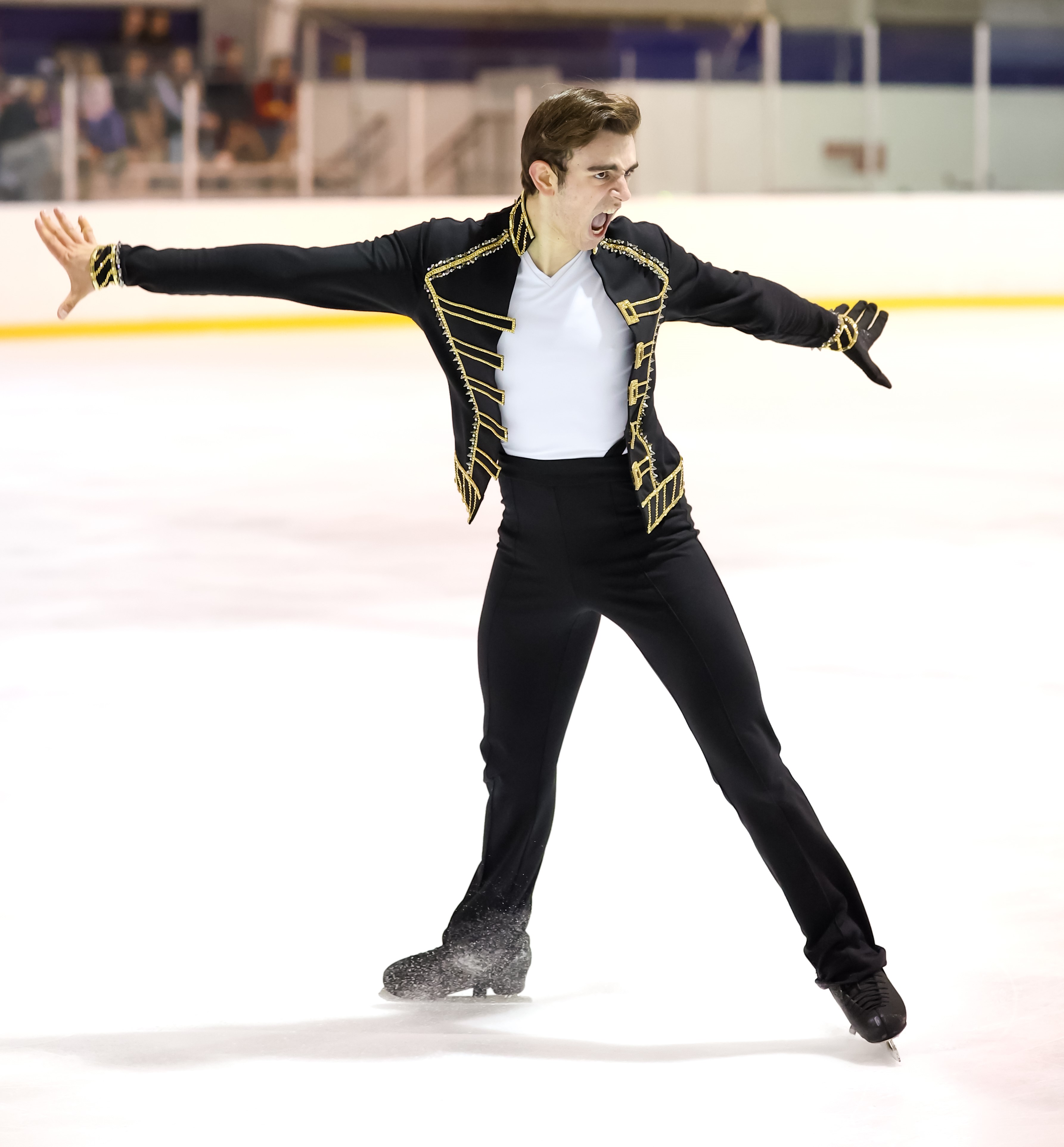 Lucas Appel skates with his arms extended and a determined look on his face. He has short brown hair and is wearing a black and gold jacket over a white shirt and black pants