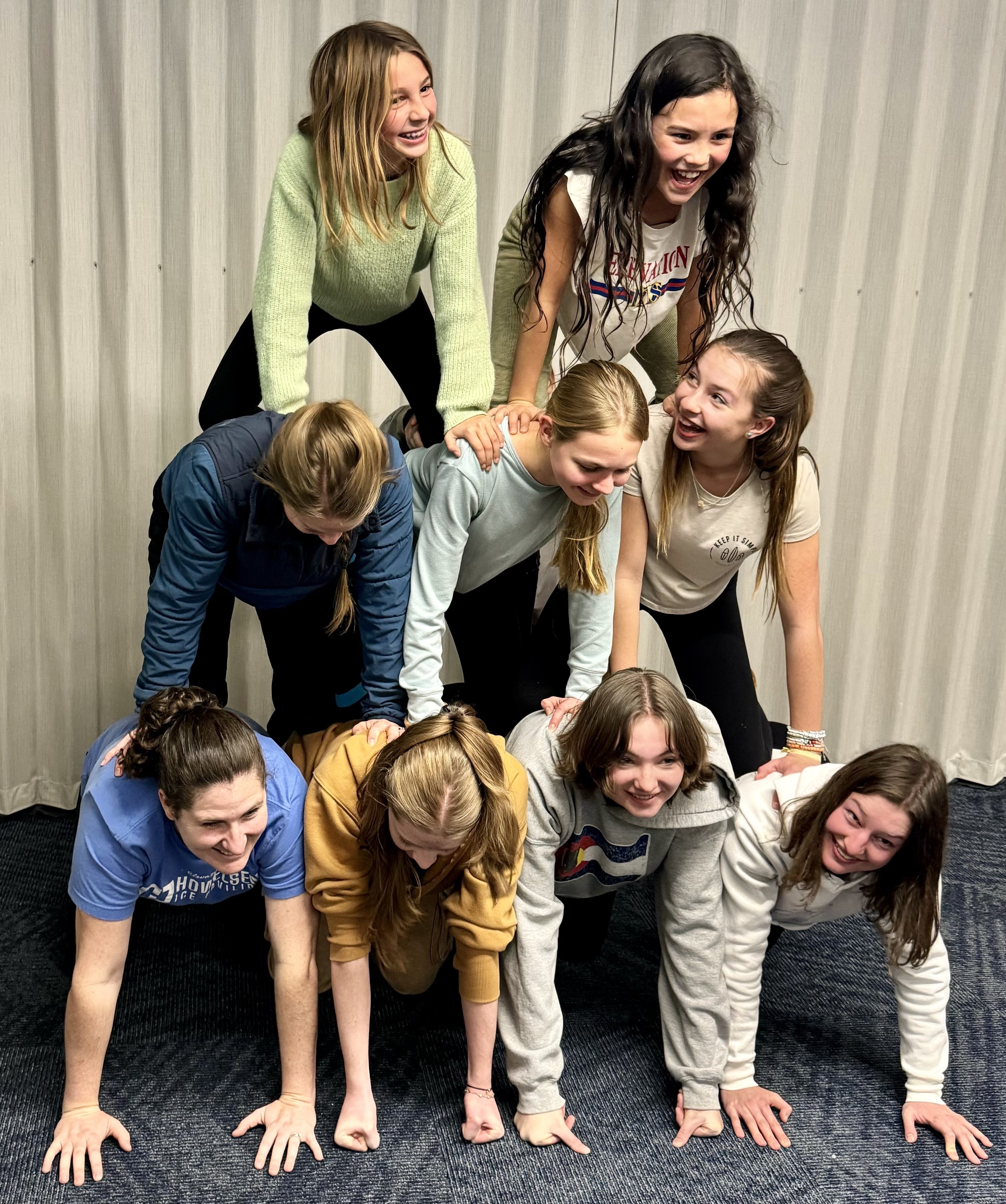 A group of skaters form a human pyramid by climbing on each others back. Some are looking down while others are smiling at each other
