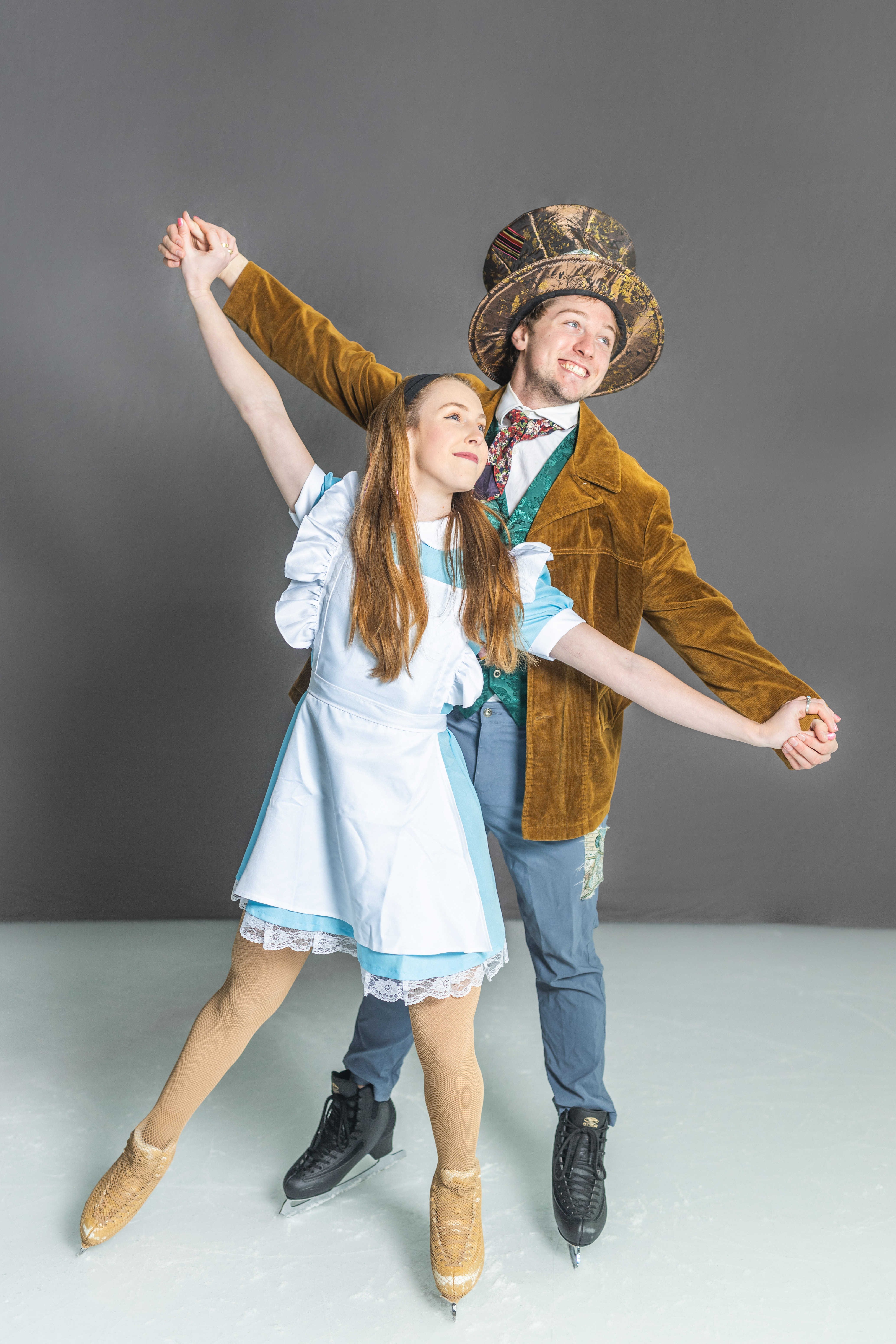 A skater dressed as Alice in Wonderland and a skater dressed as the Mad Hatter hold hands in a skating pose.