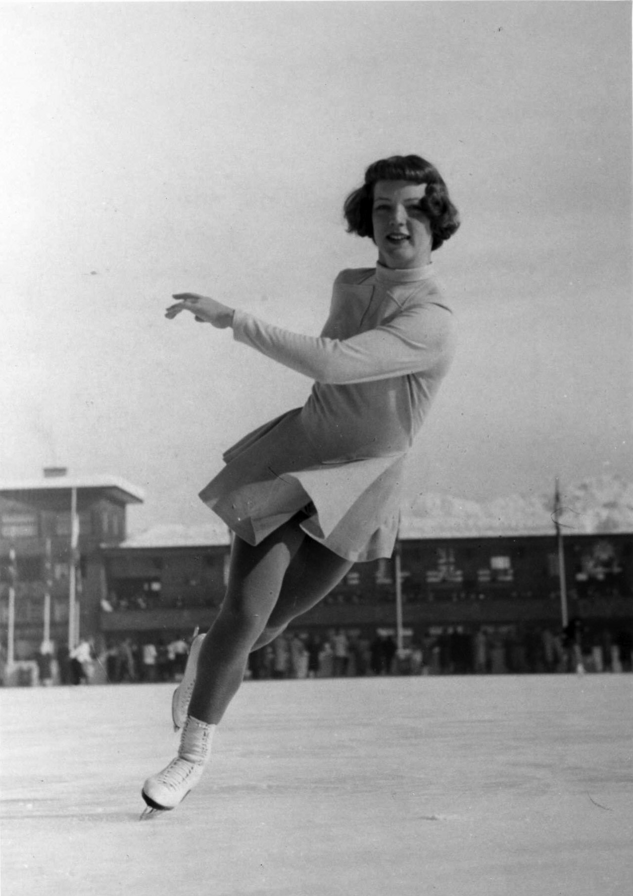 Tenley Albright skates away from the camera in a black and white photo on an outdoor frozen pond.