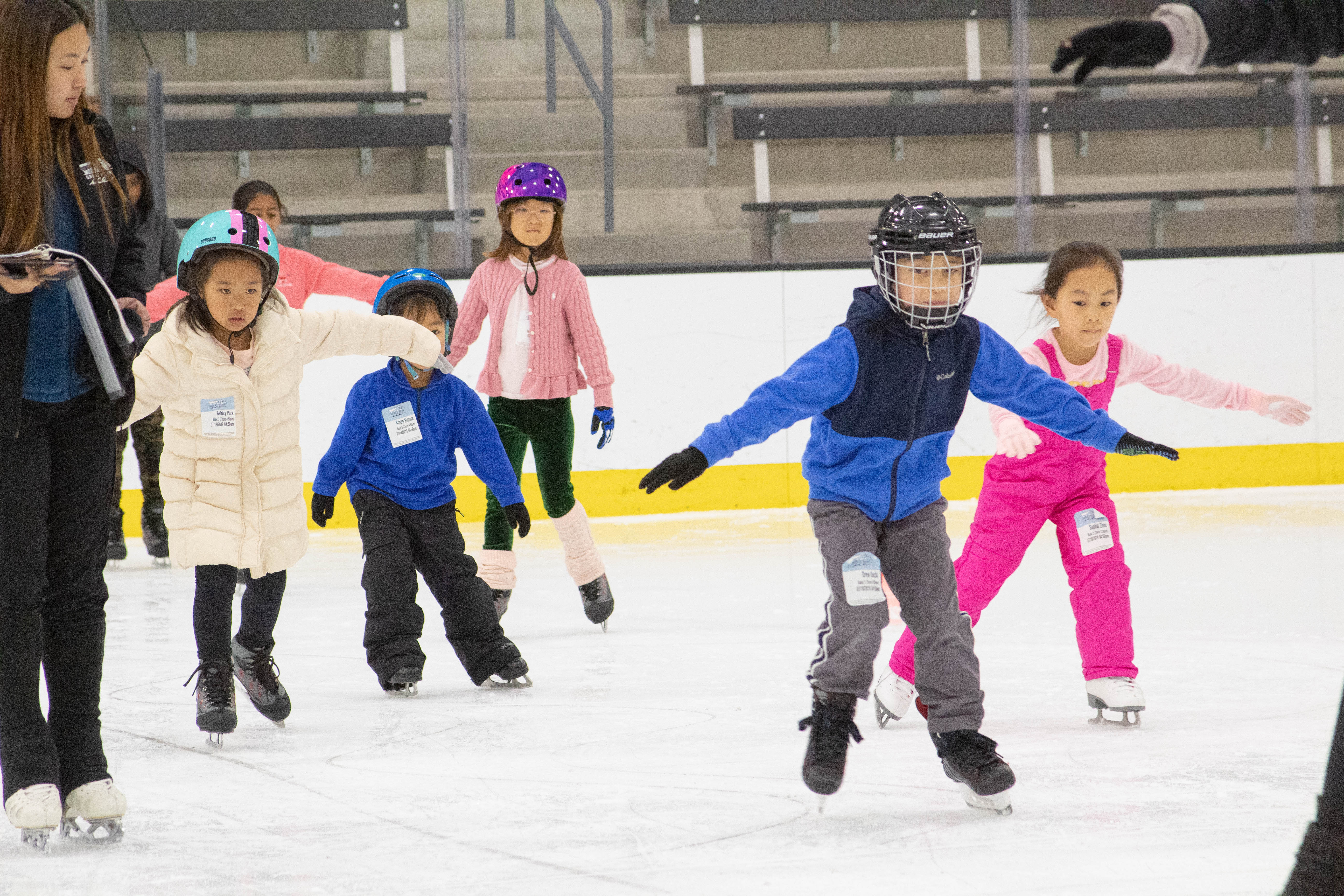 Six young children, dressed in coats and helmets, take a lesson from an instructor.
