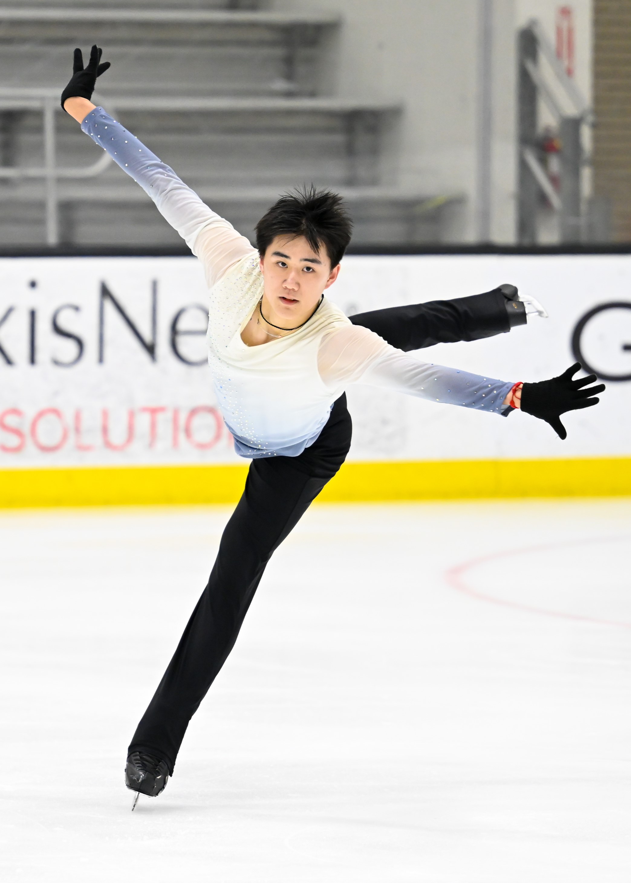 Michael Xie hands a jump on one leg with his arms outstretched. He is a young asian man wearing a blue and white long sleeve top with black pants