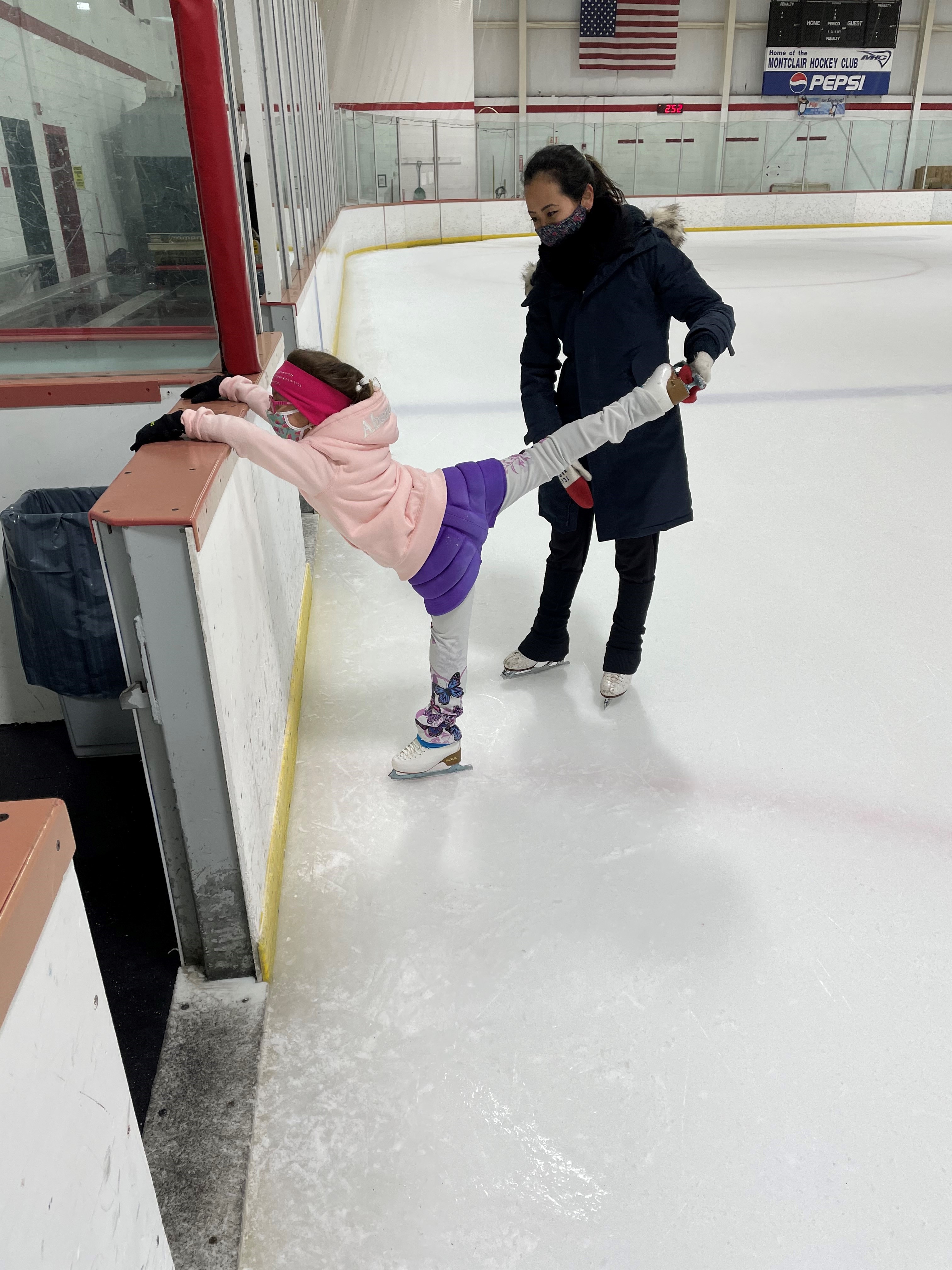 Felicia Zhang helps a young skater stretch her spiral while holding onto the boards.