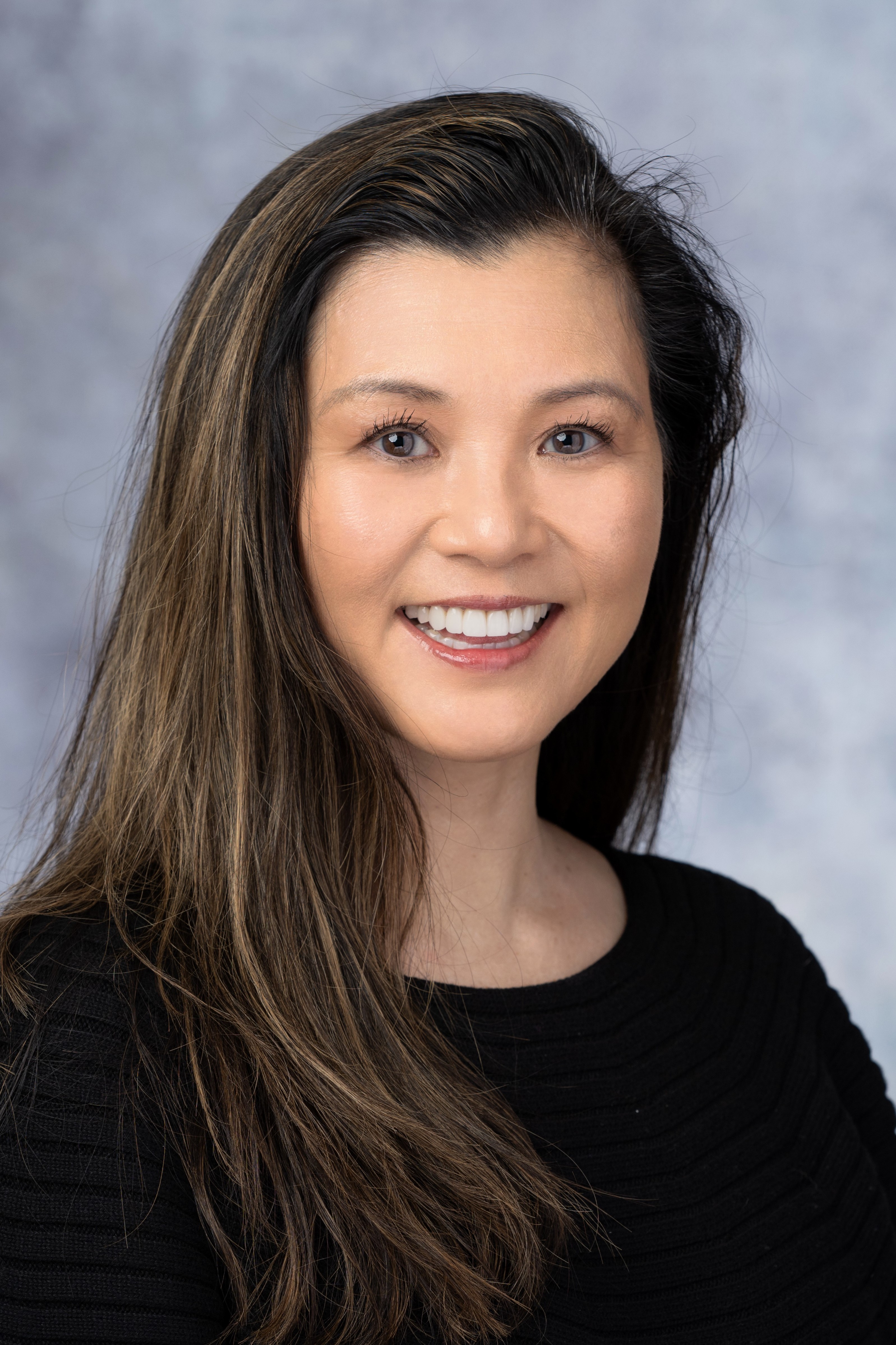 Headshot of Kyoko Ina. She is an Asian woman with long brown hair. She is wearing a black shirt 