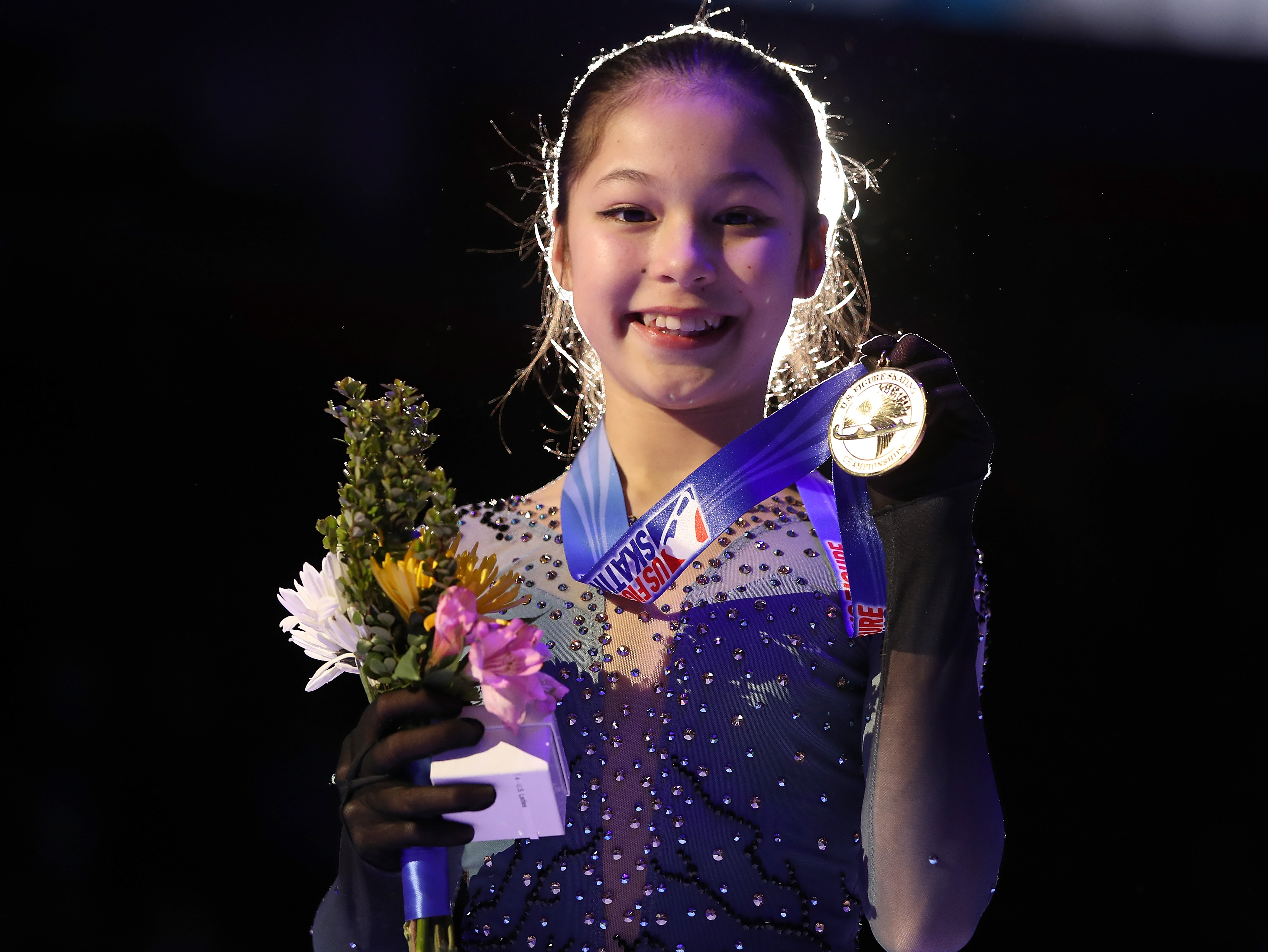 Alysa Liu holds up a U.S. Championship medal under dark lighting.
