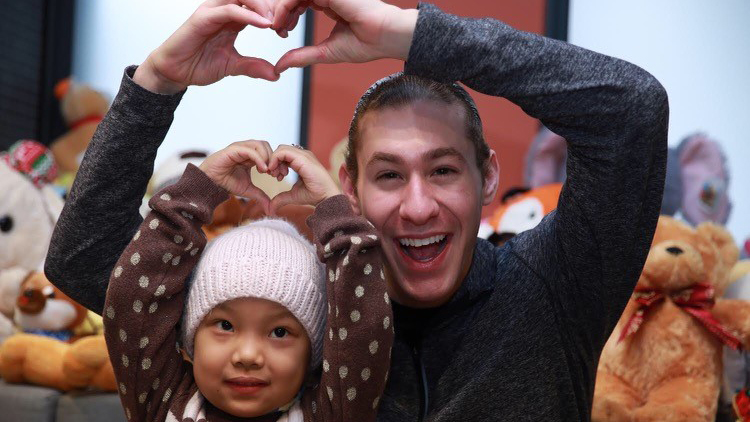 Jason Brown poses with child at Ronald McDonald House making a heart with their hands