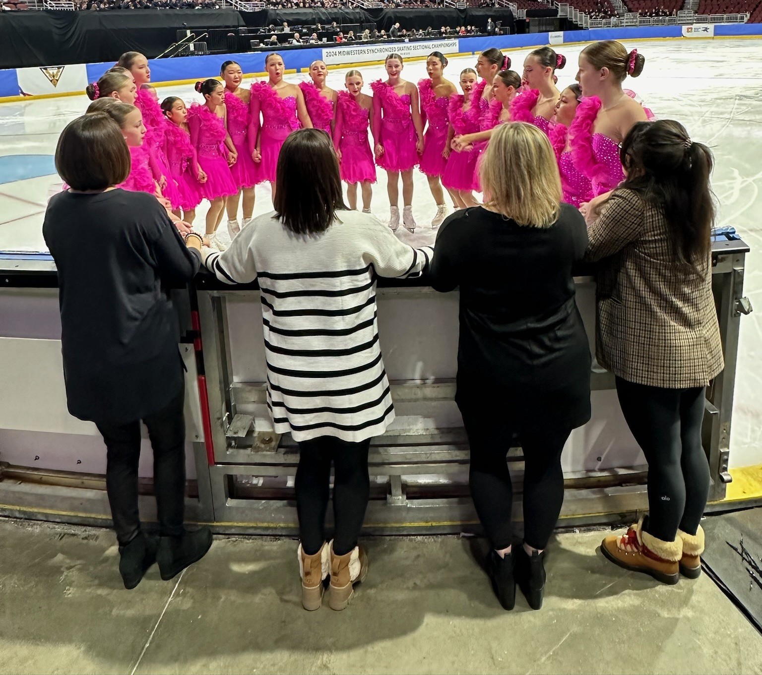 Danielle stands in a circle with her team wearing pink skating costumes