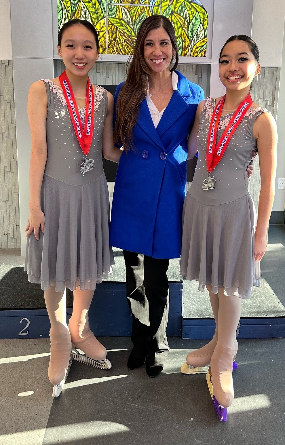 Naomi Lang (center) poses with two skaters wearing medals around their neck from the 2-23 Solo Dance Finals