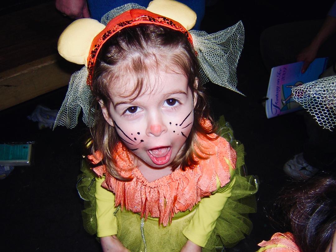 A young Angela Martino dressed as an animal with face paint and sticking her tongue out.