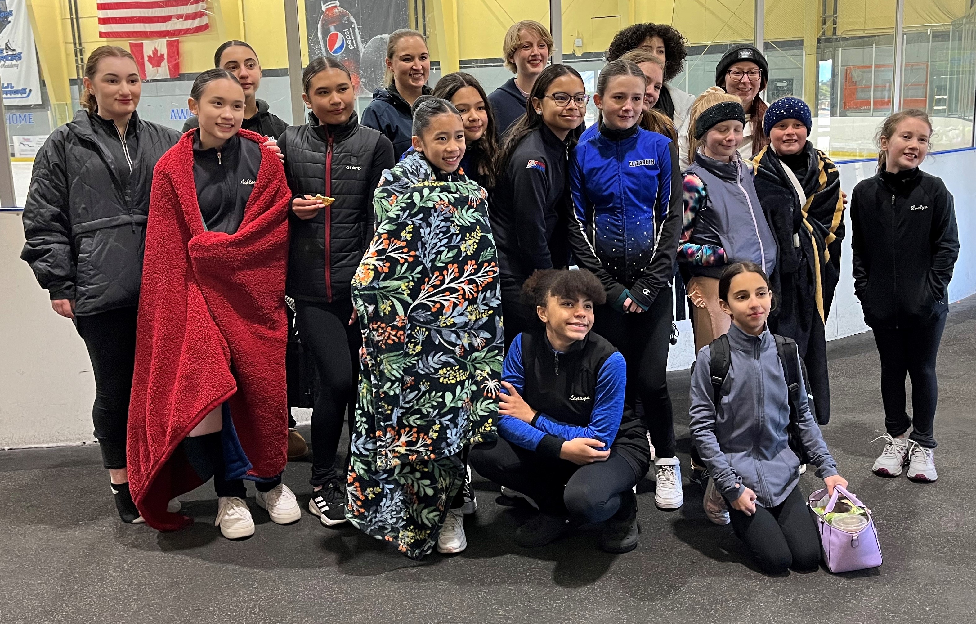 A group of young girls pose for a photo next to the rink after a successful synchronized skating clinic