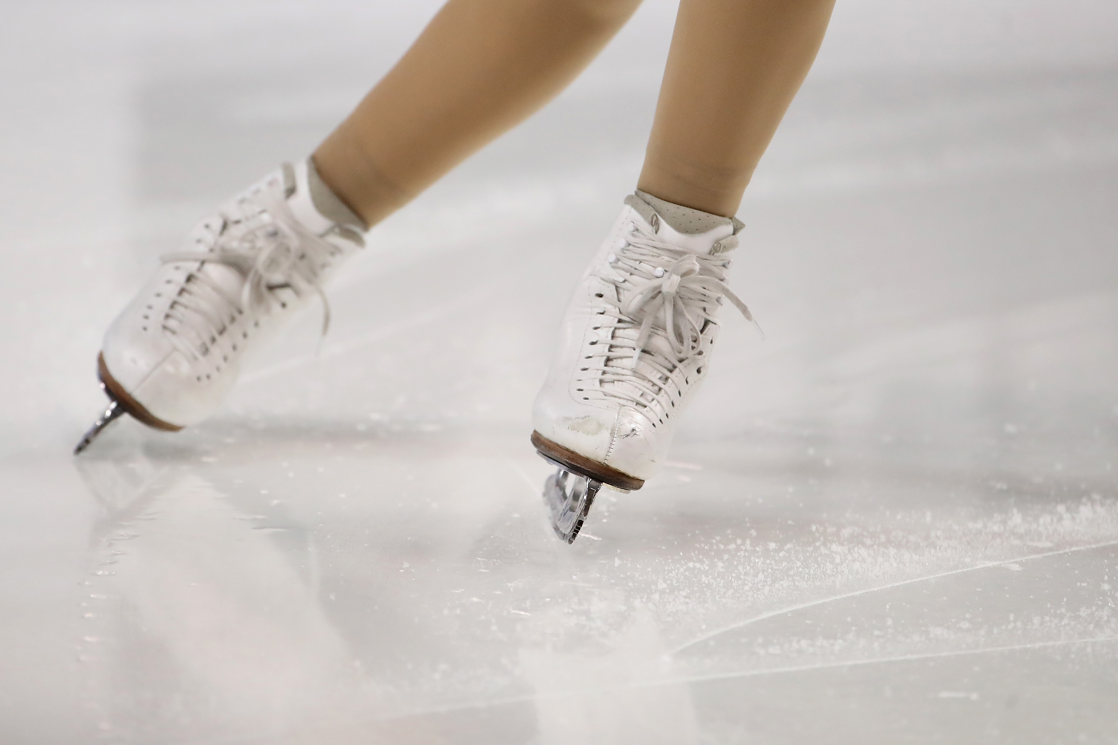 Photo of a skaters legs on the ice wearing white skates.
