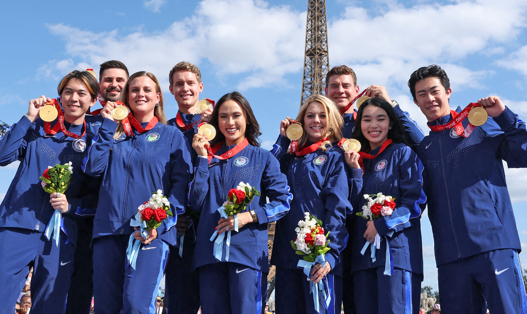 Team USA smiles with their gold medals from the 2022 Winter Olympics. They are all wearing navy blue Nike jackets and matching pants