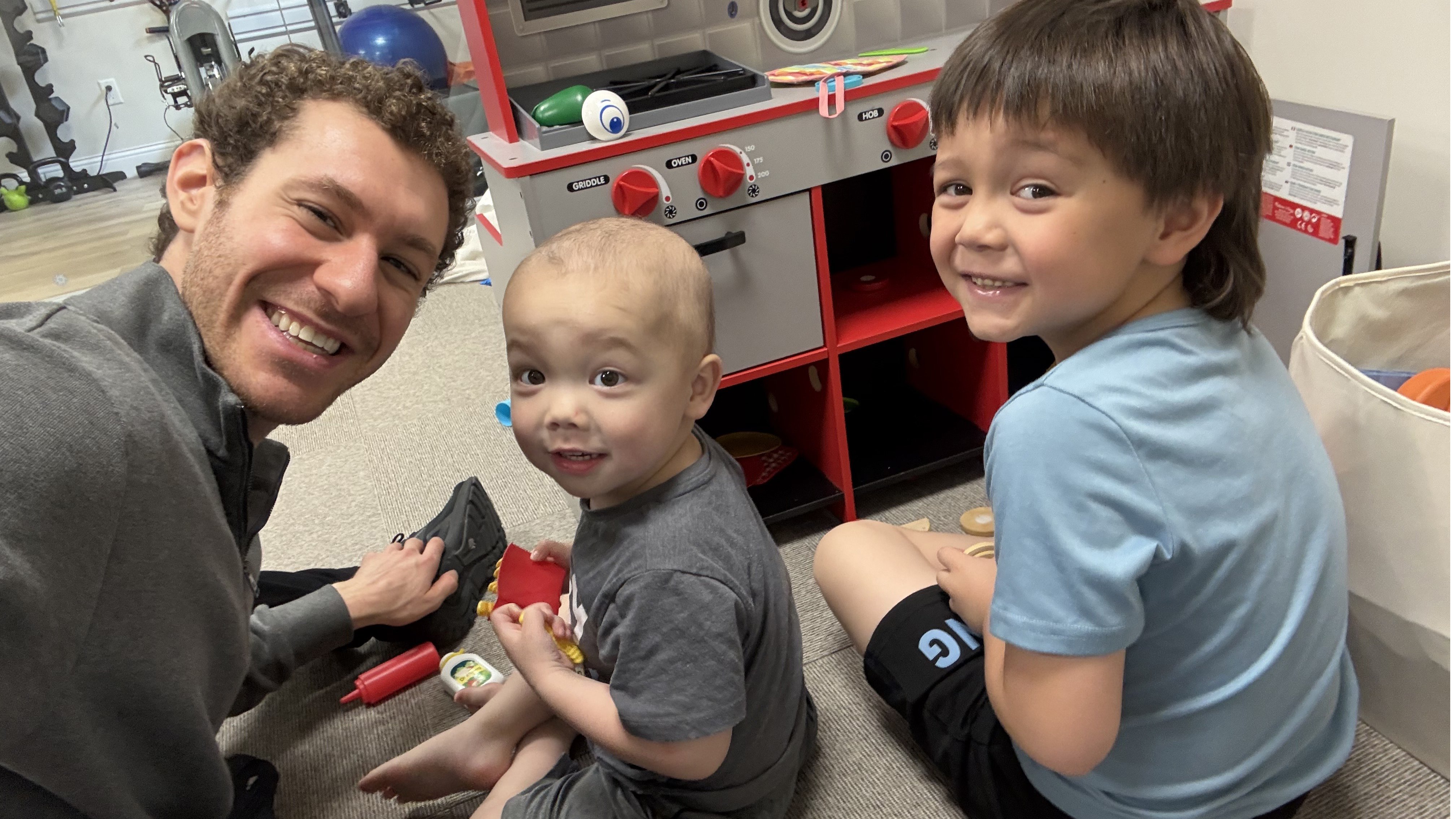 Jason Brown, with a big smile, sits on the floor and plays games with a couple of kids at one of the Ronald McDonald Houses. 