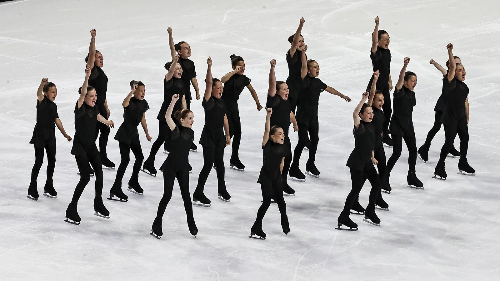 Skaters stand with one arm raised eith smiles on their faces. They are all wearing matching black costumes