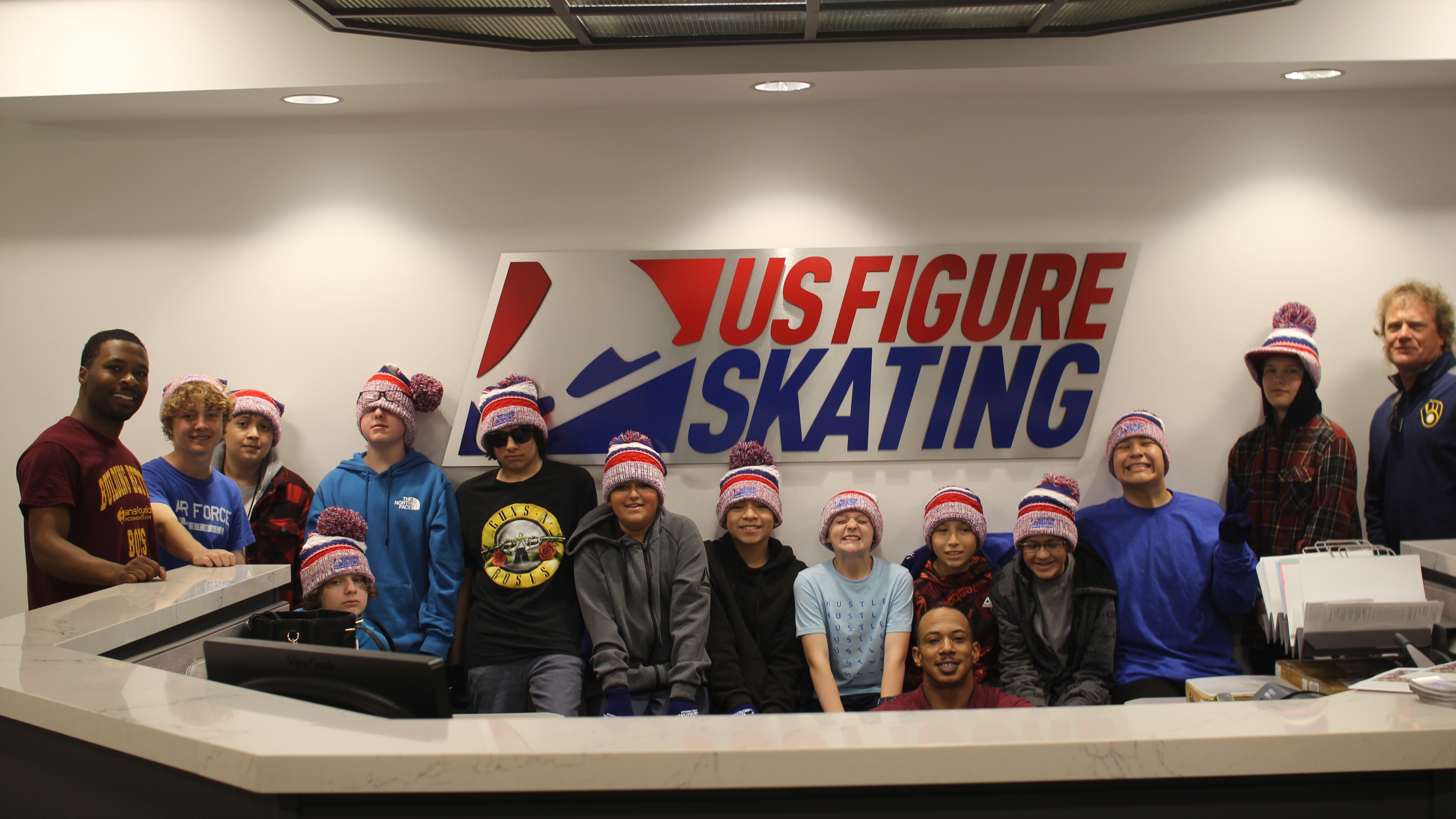 The group of students representing the Sims-Fayola Foundation stand in front of a U.S. Figure Skating sign at the U.S. Figure Skating headquarters