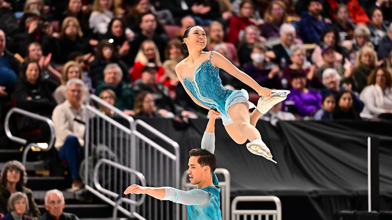 Dressed in light green, Balazs Nagy lifts Audrey Shin with one arm above his head.