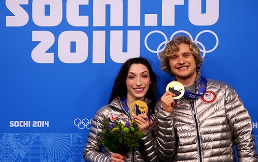 Meryl Davis and Charlie White pose with their Olympic gold medals in front of a Sochi 2014 banner.