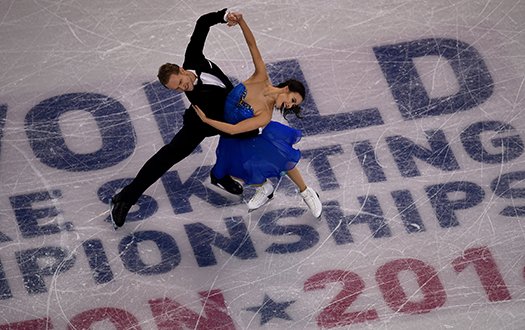 Madison Chock and Evan Bates perform a dance move over the in-ice event logo at the World Championships