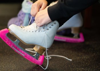 close up of a girl tying up her white figure skates with pink skate guards on them. 