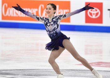 Isabeau Levito in a white and purple dress with her arms out during her routine, smiling.
