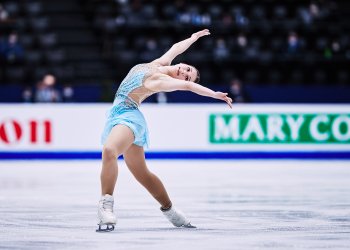 Alysa Liu streches her arms high as she skates in a blue dress at the World Championships