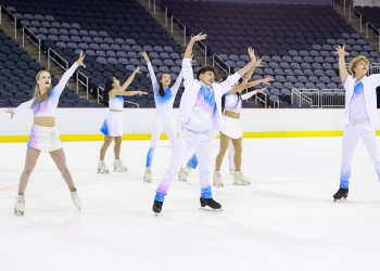 Act 1 of Boston performs wearing matching blue and white costumes. They all stand with their arms in the air