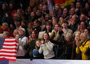 Photo of the crowd cheering at an event. One person in the front row is holding a U.S. flag
