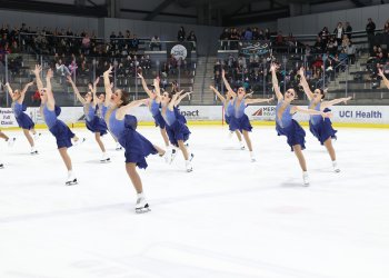 The fon du lac blades compete wearing matching purple costumes. All of the skaters skate forward smiling with their arms in the air