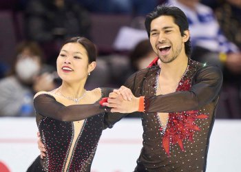 Taken from the waist up, Emily Chan and Spencer Howe in hold during their performance. They both smile, wearing black with red accents.