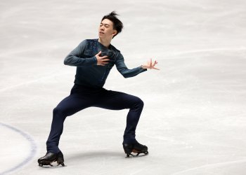Vincent Zhou in a high spread eagle wearing navy clothing on the ice.