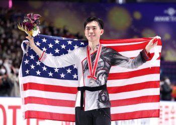 Vincent Zhou holds up the American flag with a silver medal draped around his neck. 