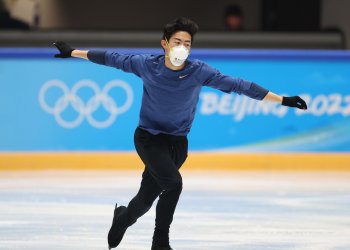 Nathan Chen skates in practice with a blue shirt and Olympic rings in the background