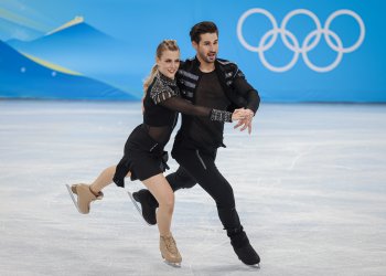 Madison Hubbell and Zachary Donohue during the team event rhythm dance with the Olympic rings on the boards behind them in Beijing.